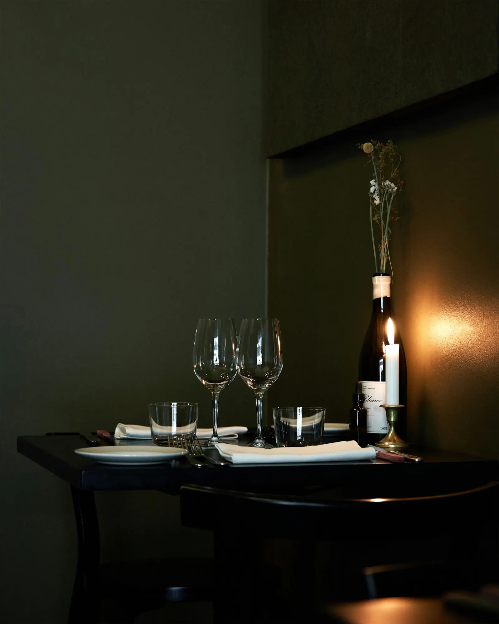 A candlelit table with wine glasses, linen and a flower-filled bottle